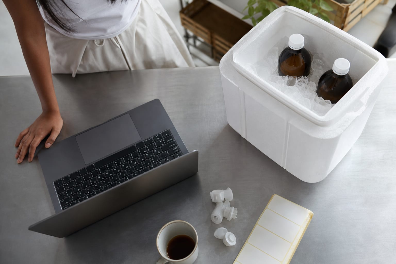Vista de cima de uma mesa com notebook aberto, pilha de folhas impressas presas por clipe e xícara de café.
